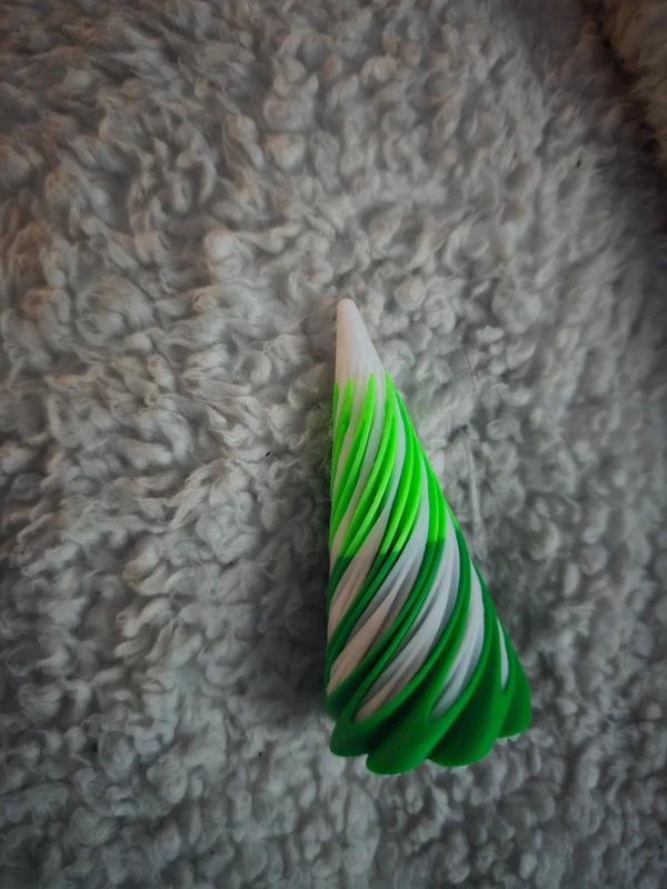 Cone-shaped Christmas fidget spinner with green and white spiral design, placed on soft textured fabric—festive sensory toy for holiday gifting.